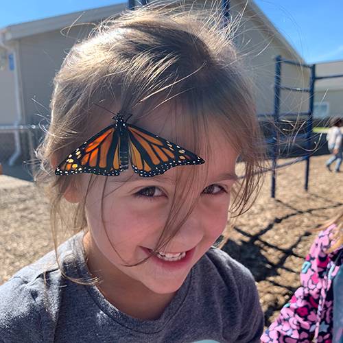 A young girl smiling as a butterfly lands on her forehead